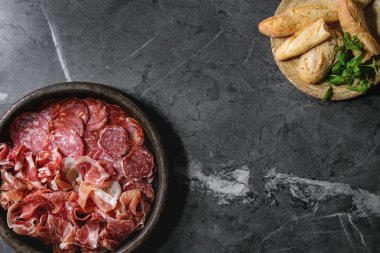 Meze et tabağı assorti dilimlenmiş jamon, salam, chorizo sosis ekmek ve yeşillik üzerinde siyah mermer zemin ile pişmiş toprak tepsisinde. Düz lay, uzay