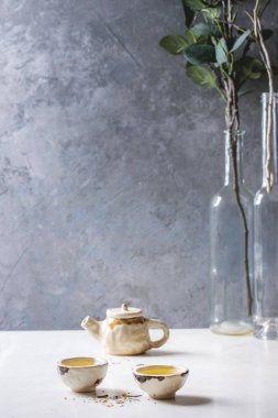 Sıcak yeşil çay iki geleneksel Çin Kil seramik Kupası ve beyaz mermer masada duran çaydanlık. Yeşil şubesine arka plan.