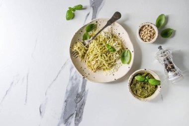 Pesto sos, çam fıstığı, zeytin yağı ve taze fesleğen ile klasik İtalyan spagetti makarna. Seramik tabak çatal ve malzemeler yukarıda beyaz mermer arka plan üzerinde servis. Düz lay, uzay