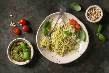 Pesto sos, çam fıstığı, zeytin yağı ve taze fesleğen ile klasik İtalyan spagetti makarna. Seramik tabak çatal ve malzemeler yukarıda karanlık metal arka plan üzerinde servis. Düz lay, uzay