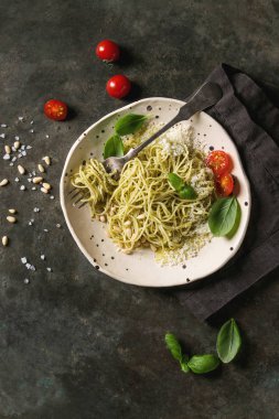 Pesto sos, çam fıstığı, zeytin yağı ve taze fesleğen ile klasik İtalyan spagetti makarna. Seramik tabak çatal ve malzemeler yukarıda karanlık metal arka plan üzerinde servis. Düz lay, uzay