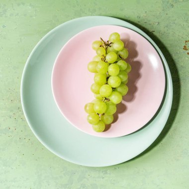 Yeşil pastel pin-up arka plan üzerinde turkuaz plaka üzerinde olgunlaşmış yeşil üzüm demet. Uzay kopyalayın. Üstten görünüm. Kare görüntü