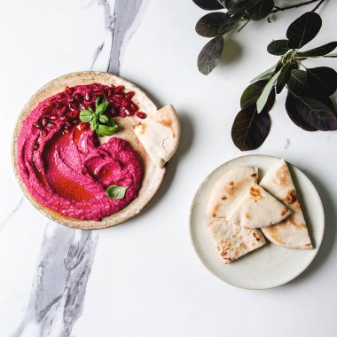 Ev yapımı yayılan kırmızı pancar humus nar taneleri, zeytin yağı, fesleğen ile beyaz mermer arka plan üzerinde pide ekmek ve yeşil Şubesi ile seramik plaka üzerinde görev yaptı. Düz lay, alan. Kare görüntü