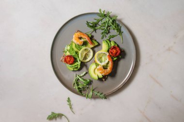 Vejetaryen sandviç dilimlenmiş avokado, Güneş kurutulmuş domates, karides, roka ile seramik beyaz mermer arka plan üzerinde tabakta. Düz lay, uzay