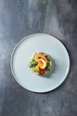 Vejetaryen sandviç doğranmış avokado, Güneş kurutulmuş domates, yumurta, karides, krem peynir ile seramik mavi doku arka plan üzerinde tabakta. Düz lay, uzay