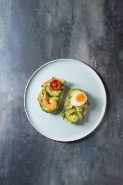 Vejetaryen sandviç ile dilimlenmiş avokado, domates, yumurta, karides, mavi doku arka plan üzerinde seramik tabakta kurutulmuş. Düz lay, uzay