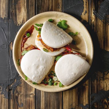 Asya sandviç Gua bao buns domuz eti, yeşil ve koyu ahşap tahta arka plan üzerinde seramik tabak içinde servis sebze ile atmak. Asya tarzı hızlı yiyecek yemek. Düz yatıyordu. Kare görüntü