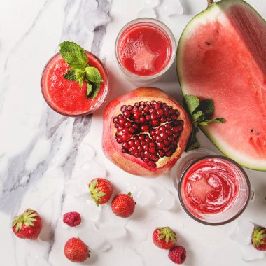 Üç farklı kırmızı meyve meyve karpuz, çilek, ahududu, nar kokteyl veya smoothies gözlük kırılmış buz ile taze nane. Beyaz mermer zemin. Düz yatıyordu. Kare görüntü