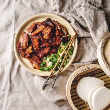 Çince Geleneksel çanak Kanton Barbekü domuz eti taze soğan ile keten kumaş üzerinde yemek çubukları, bambu vapur ve gua bao otobüs ile seramik tabak içinde görev yaptı. Düz lay, alan. Kare görüntü