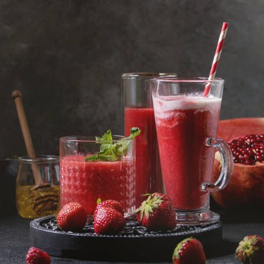Üç farklı kırmızı meyve karpuz, çilek, ahududu, nar kokteyl veya ezilmiş buz, nane ve siyah tablo yukarıda malzemeler ile bardaklarda smoothies berry. Kare görüntü