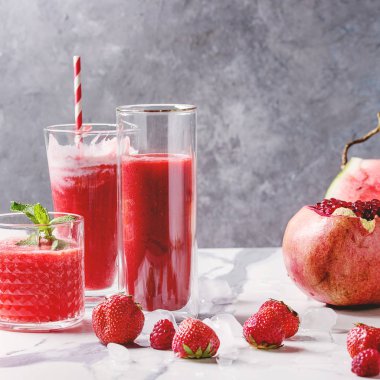 Üç farklı kırmızı meyve karpuz, çilek, ahududu, nar kokteyl veya ezilmiş buz ve beyaz mermer tablo yukarıda malzemeler ile bardaklarda smoothies berry. Kare görüntü