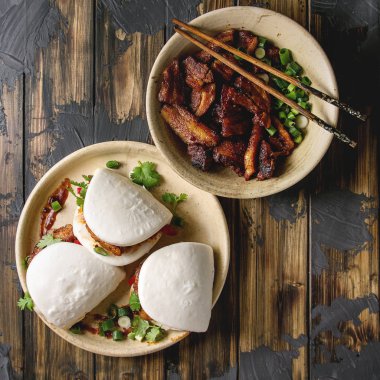 Asya sandviç Gua bao buns domuz eti, yeşil ve koyu ahşap tahta arka plan üzerinde seramik tabak içinde servis sebze ile atmak. Asya tarzı hızlı yiyecek yemek. Düz yatıyordu. Kare görüntü