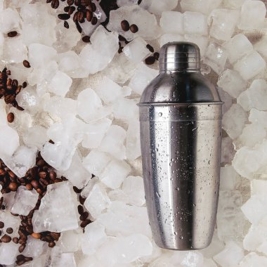 Kahve kokteyl frappe kavram yapma. Gümüş shaker ve ezilmiş buz küpleri üzerinden kavrulmuş kahve çekirdekleri. Düz lay, alan. Kare görüntü