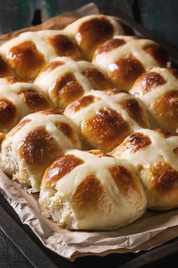 Ev yapımı Paskalya geleneksel hot cross buns fırın tepsisindeki kağıt koyu ahşap arka plan üzerinde pişirme ile. Yakın çekim
