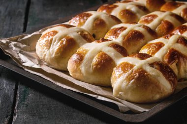 Ev yapımı Paskalya geleneksel hot cross buns fırın tepsisindeki kağıt koyu ahşap arka plan üzerinde pişirme ile. Yakın çekim