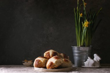 Ev yapımı Paskalya geleneksel hot cross buns nergis çiçek ve keten masa örtüsü üzerinde tavşan dekor seramik tabak ayakta. Kopya alanı.