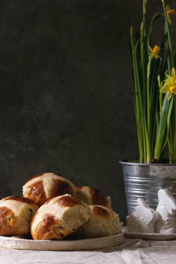 Ev yapımı Paskalya geleneksel hot cross buns nergis çiçek ve keten masa örtüsü üzerinde tavşan dekor seramik tabak ayakta. Kopya alanı.