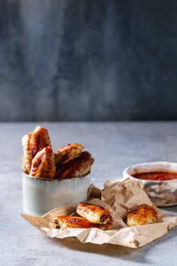 Barbekü baharatlı tavuk kanadı seramik kase ve kağıt üzerinde ışık mavi masada kırmızı sos ile servis.