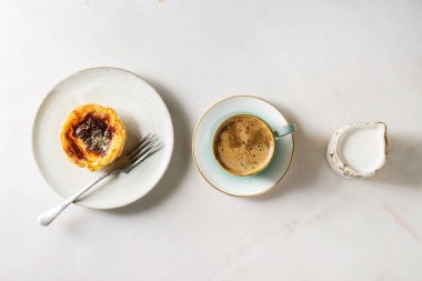 Geleneksel Portekizce tart tatlı Pasteis Pastel de nata seramik plaka üzerinde beyaz mermer zemin çatal, siyah kahve ve krem satırda sürahi ile yumurta. Düz lay, uzay