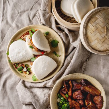 Asya sandviç gua bao buns domuz eti, yeşil ve seramik tabak içinde keten masa örtüsü üzerinde hizmet sebze ile atmak. Asya tarzı hızlı yiyecek yemek. Düz lay, alan. Kare görüntü