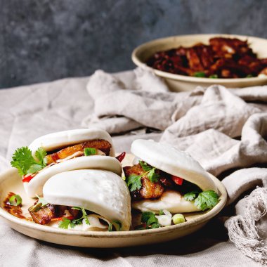 Asya sandviç gua bao buns domuz eti, yeşil ve sebzeler ile keten masa örtüsü seramik tabak masaya servis ile atmak. Asya tarzı hızlı yiyecek yemek. Kare görüntü