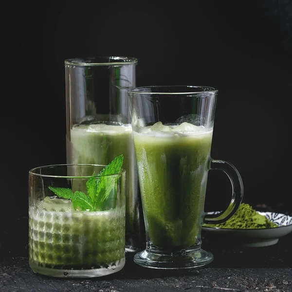 Matcha yeşil çay kahve veya kokteyl nane, buz küpleri ve karanlık doku arka plan üzerinde tozu matcha ile üç farklı bardaklarda buzlu. Kare görüntü
