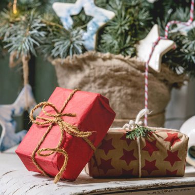 Noel süslemesi köknar ağacı dalları, seramik yıldızlar, parlak çelenkler, arka planda ahşap kapılı klasik beyaz sandalyede el işi kağıt kutular. Noel ve Yeni Yıl İçi.