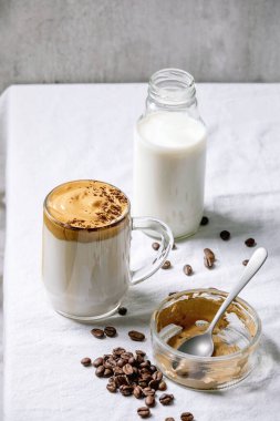 Dalgona köpüklü kahve trend Kore sütlü latte, cam bardak köpüklü, öğütülmüş kahve ile süslenmiş beyaz pamuk masa örtüsü. Yukarıdaki İçindekiler