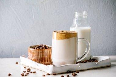 Dalgona köpüklü kahve trend Kore sütlü latte, cam bardak köpüklü seramik tepside beyaz mermer masa malzemeleri..