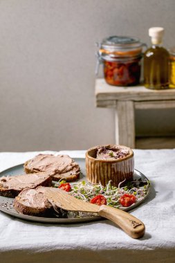 Sandviç ve ev yapımı tavuk ciğeri ezmesi, ahşap bıçaklı, güneşte kurutulmuş domatesler ve gri tabakta yeşil filizli salata beyaz keten masa örtüsü. Evde kahvaltı ya da aperatif.