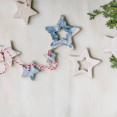 Noel dekorasyon seramik yıldızları beyaz ve mavi kaplamalı, farklı boyutlarda, beyaz mermer zemin üzerinde yeşil dallar. Noel ve Yeni Yıl tebrik kartı. Düz yat, boşluğu kopyala.