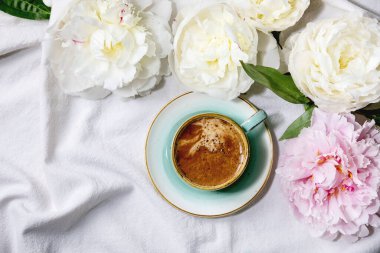 Bir fincan espresso kahve, pembe ve beyaz şakayık çiçekleri beyaz pamuk tekstil arka planında yapraklar. Düz yat, boşluğu kopyala