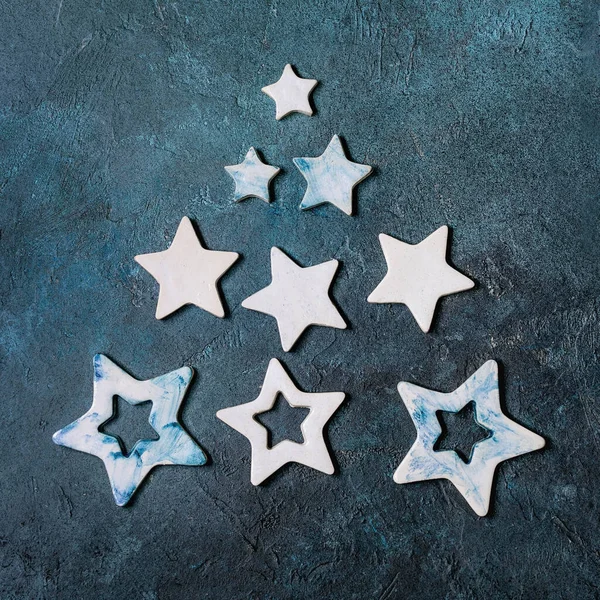Christmas decoration ceramic stars white and blue glazed, different size, as christmas tree shape over blue texture background. Christmas and New year greeting card. Flat lay, space.