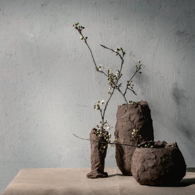 Gri masa örtüsünün üzerindeki kil vazolarda çiçek açan kiraz dalları. Bahar iç dekorasyonları.