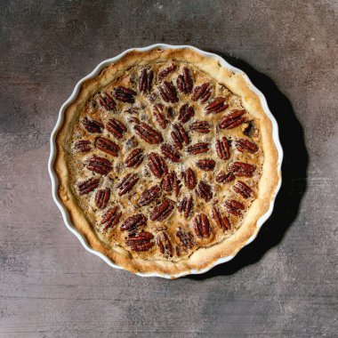 Taze ev yapımı klasik Amerikan cevizli turta, beyaz seramik fırın kabında, gri doku arka planında. Düz uzanış, boşluk