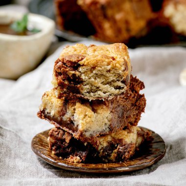 Brookies çikolatalı kekler ve kurabiyeler farklı seramik tabaklarda kareler, çikolata sosu, gri keten masa örtüsünde ahşap kaşıklar tarafından dilimlenmiş ev yapımı kekler.