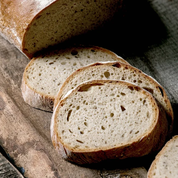 Eski ahşap zemin üzerinde dilimlenmiş tahıllı çavdar-buğday organik ekmeği. Kapat.