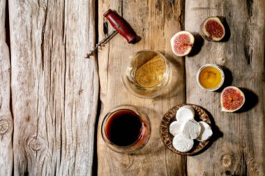 İncirli kırmızı ve beyaz şarap, keçi peyniri ve bal eski ahşap arka planda. Düz yat, boşluğu kopyala