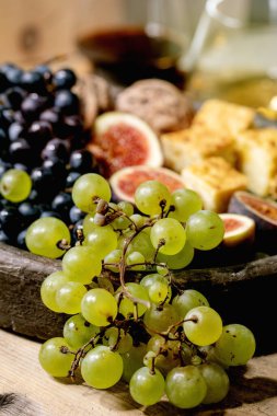 Şarap aperatifleri farklı üzümler, incir, ceviz, ekmek, bal ve keçi peyniri seramik tabakta, eski ahşap zemin üzerinde kırmızı ve beyaz şarapla servis ediliyor. Kapat.