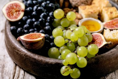 Şarap aperatifleri farklı üzüm, incir, ceviz, ekmek, bal ve keçi peyniri ile seramik tabakta eski ahşap arka planda. Kapat.