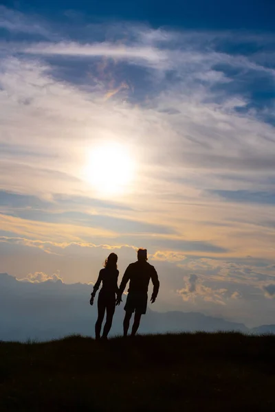 山の夕暮れカラフルな雲に向かって歩いて手を繋いでいるシルエットのカップル — ストック写真