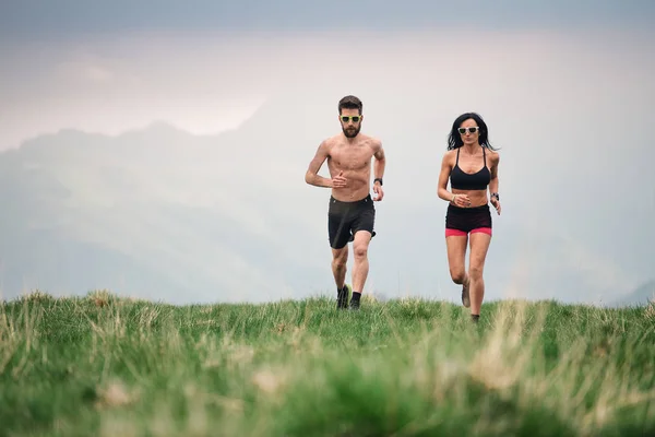 スポーティな男性と女性が丘の牧草地で夏に熱く走る — ストック写真