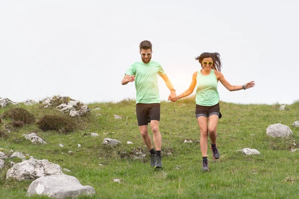 Bir çift sporcu el ele tepe çayırlarında koşar — Stok fotoğraf