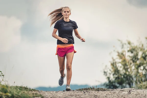 Piękna Blondynka sportowiec biegnie na polnej drodze na wzgórzach — Zdjęcie stockowe