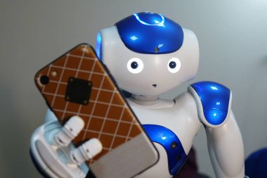 Robot telefon elinde tutuyor. Bir insan yüzü ve insansı vücut ile küçük bir robot. Yapay zeka-Ai. Mavi-beyaz robot.