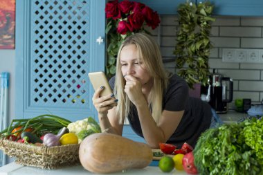 Kız mutfakta sebze ile sağlıklı yiyecek hazırlar. Seyir için bir reçete smartphone kullanarak. Vejetaryen mutfağı. Onun yirmili bir genç Avrupalı. Sağlıklı beslenme kavramı.