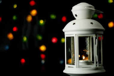 Noel beyaz fener renkli ışıklar garland, bokeh arka plan üzerinde yanan bir mum ile.
