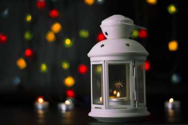 Noel beyaz fener renkli ışıklar garland, bokeh arka plan üzerinde yanan bir mum ile.