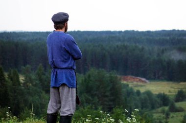 Doğada, geleneksel halk kostümlü bir genç adam mesafe içine arıyorum. Yeşil çam ormanı.