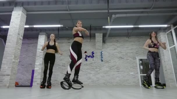 A female group of three young, sexy girls Kangoo Jumps in the gym. — Stock Video